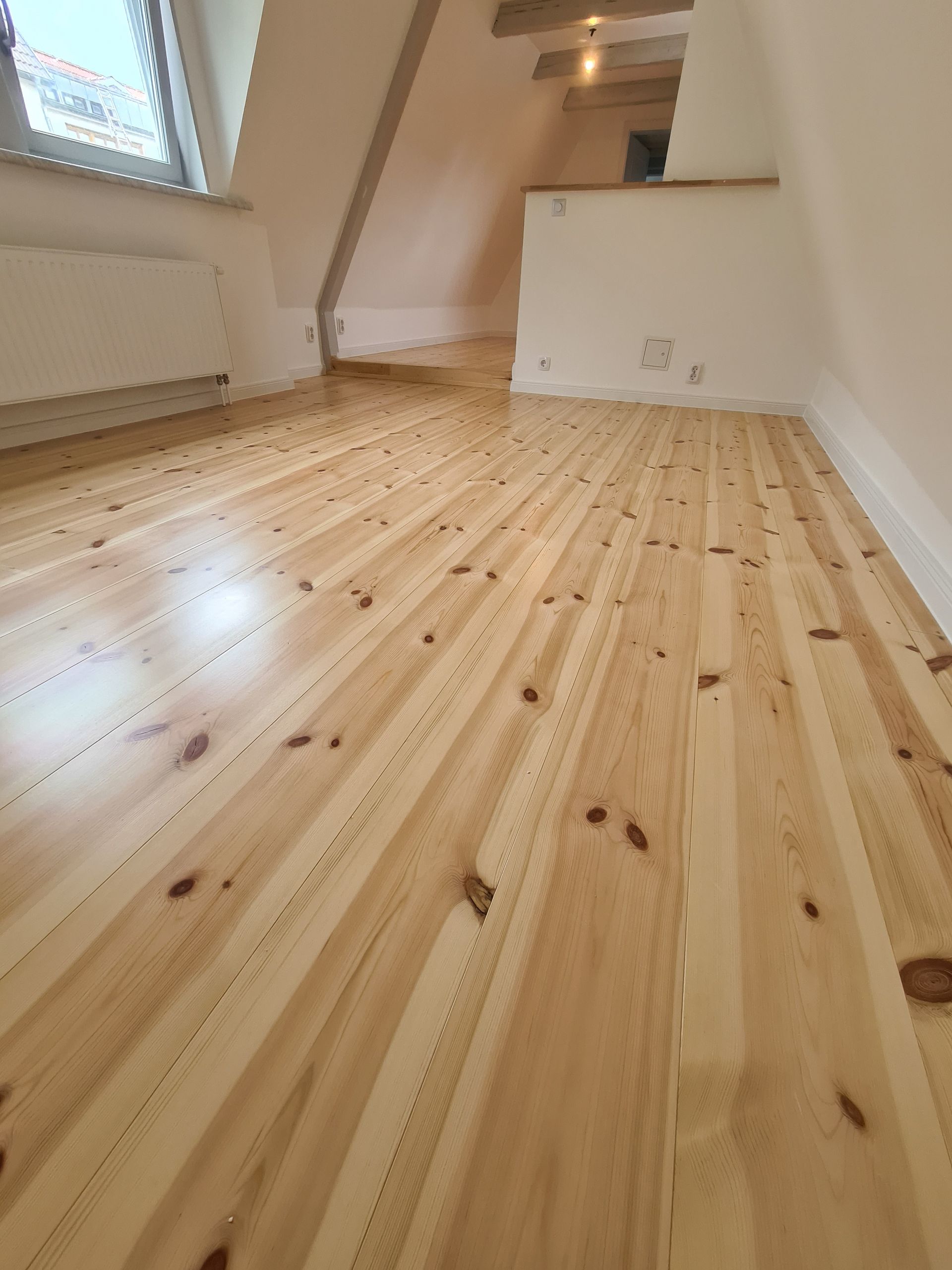 ein Wohnzimmer mit Holzboden und weißen Wänden .