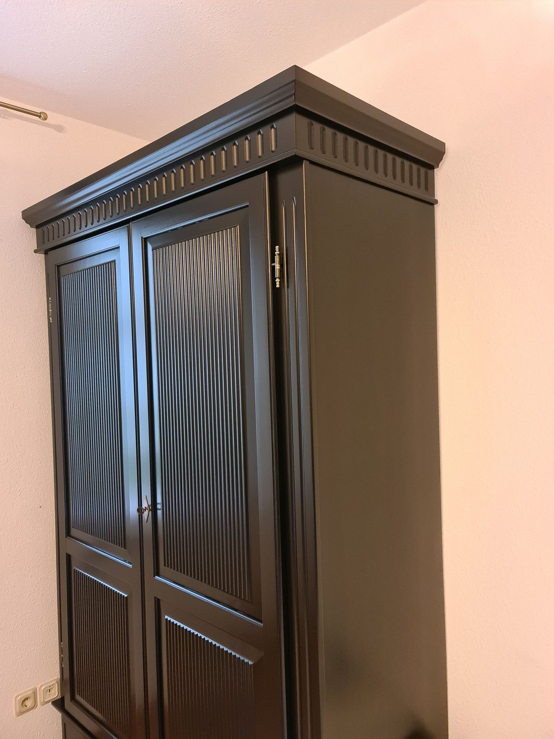ein schwarzer kleiderschrank steht in einem zimmer neben einer weißen wand