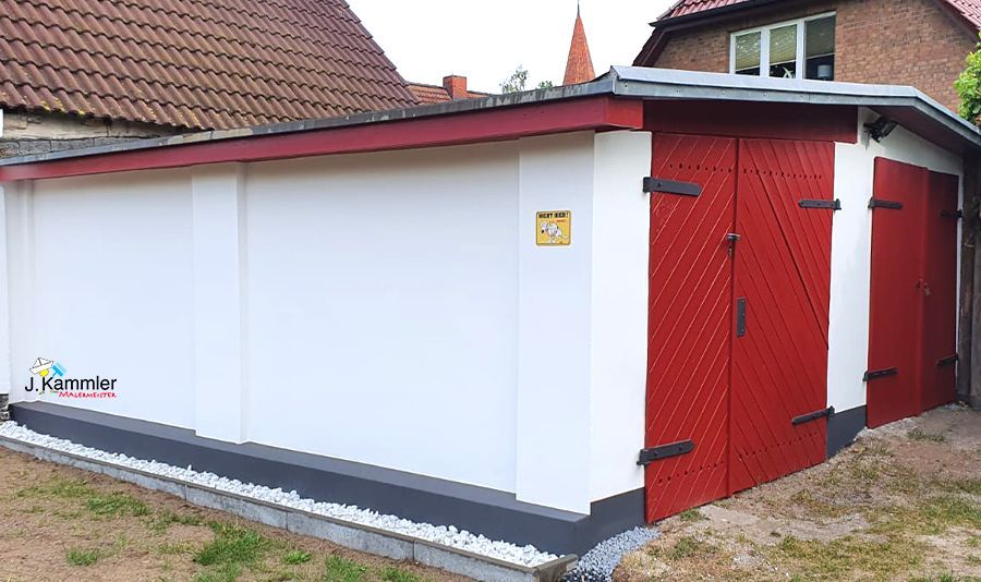 eine Garage mit roten Türen und weißen Wänden neben einem Haus .