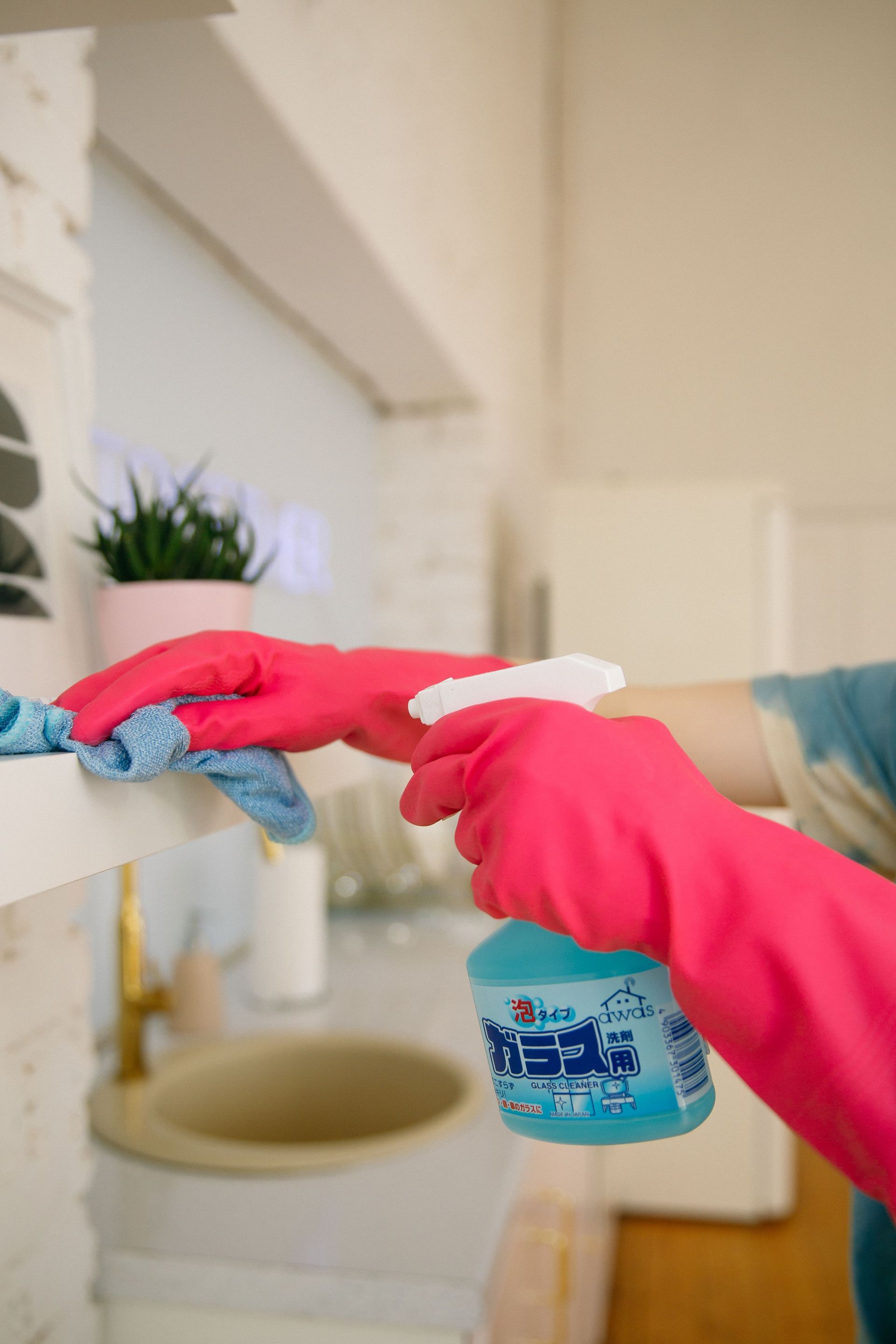 Manos enguantadas limpiando un lavabo con un pulverizador y paños.