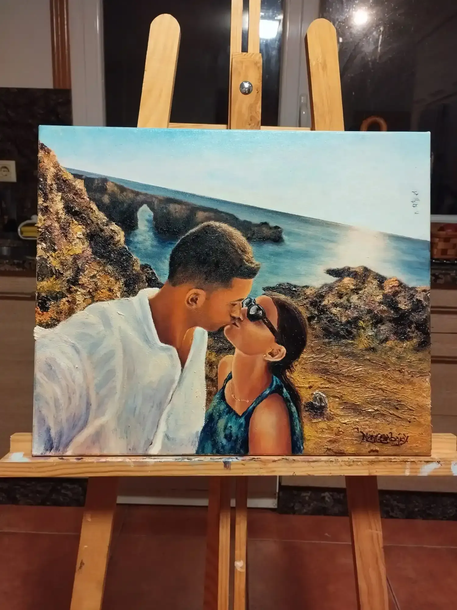 Una pareja besándose en un acantilado rocoso, con el mar azul y un cielo brillante de fondo.