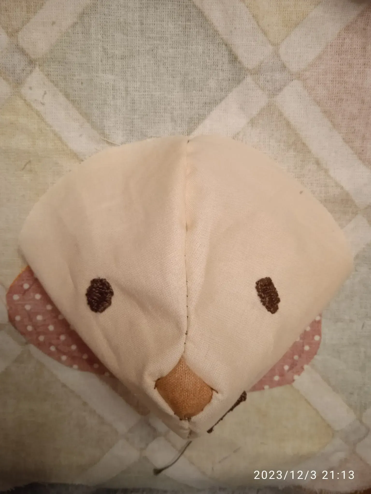 Peluche de pájaro con tela color crema, ojos oscuros y un pequeño pico naranja sobre una manta estampada.