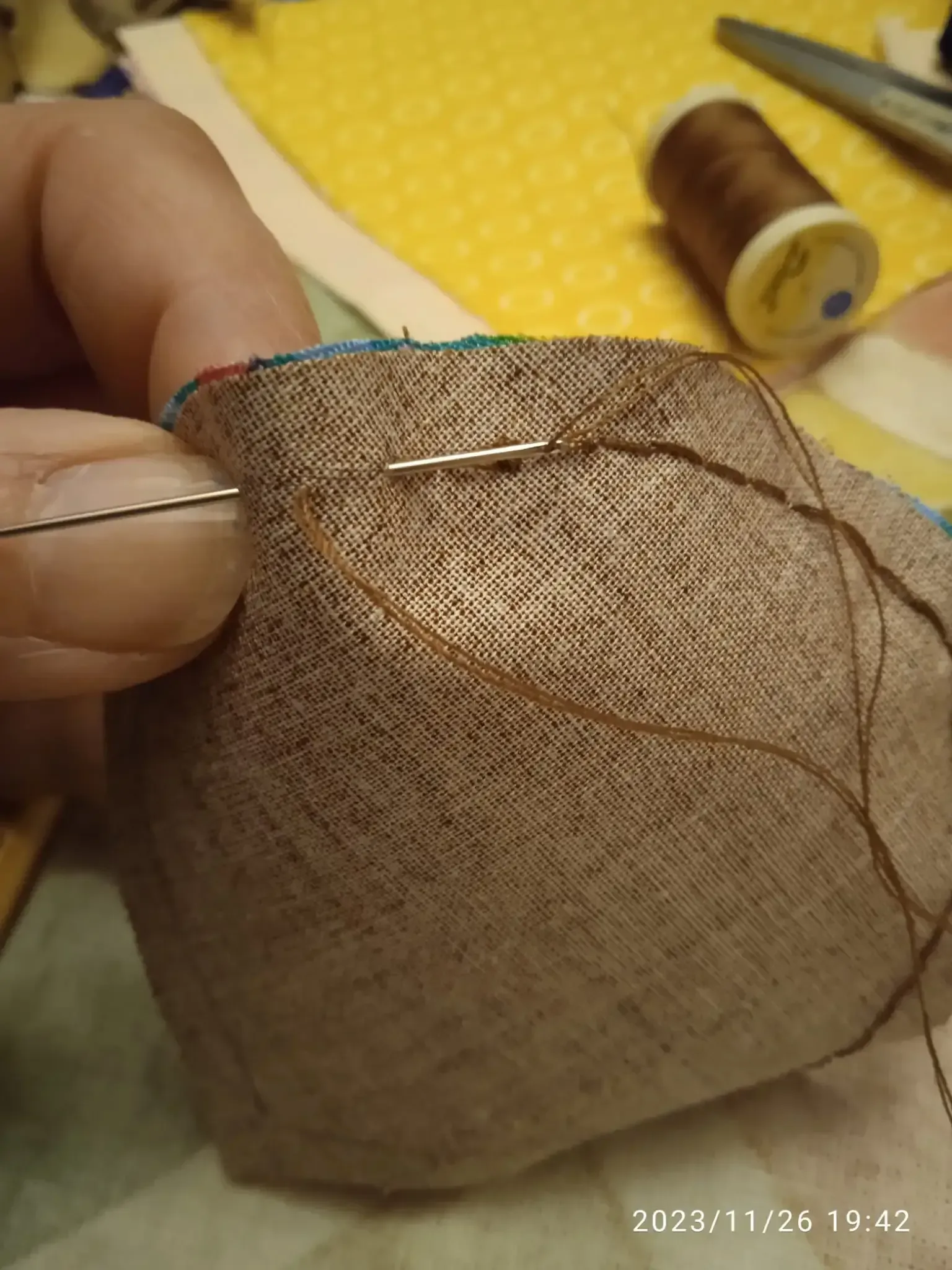 Coser a mano tela transparente marrón con aguja e hilo sobre una superficie amarilla.
