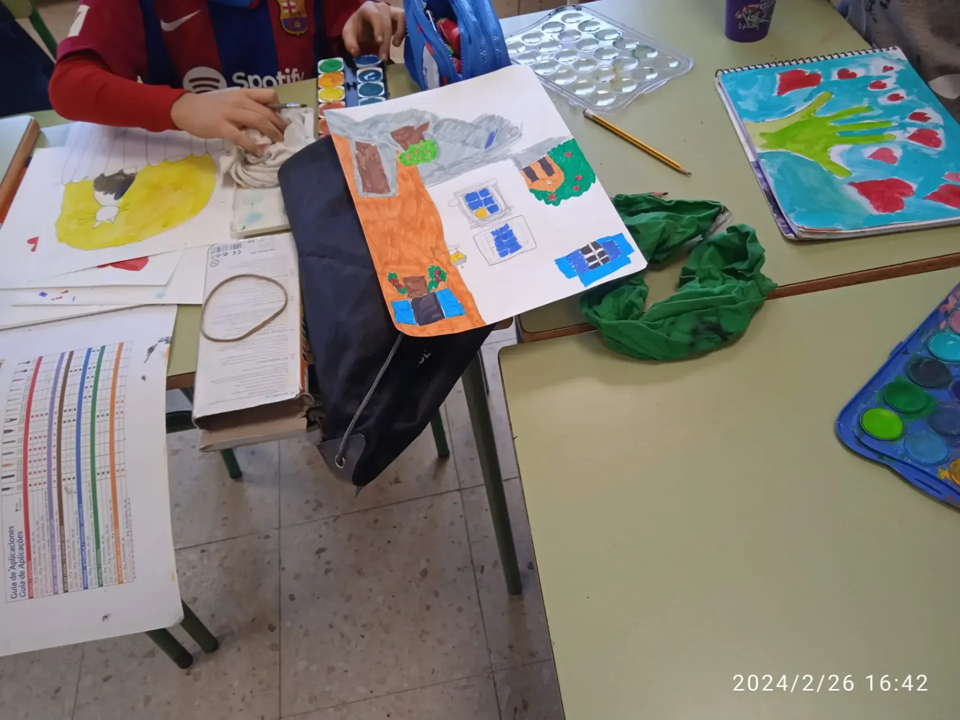 Proyectos artísticos infantiles sobre una mesa de aula con dibujos coloridos y paletas de pintura.