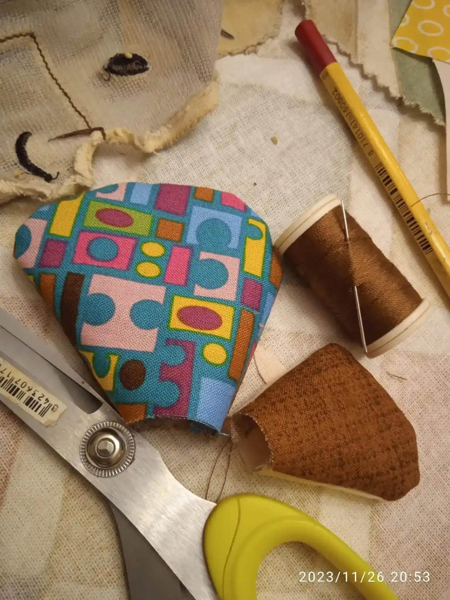 Trozos de tela con motivos geométricos de colores, tijeras, un lápiz y materiales de costura sobre una mesa de trabajo.