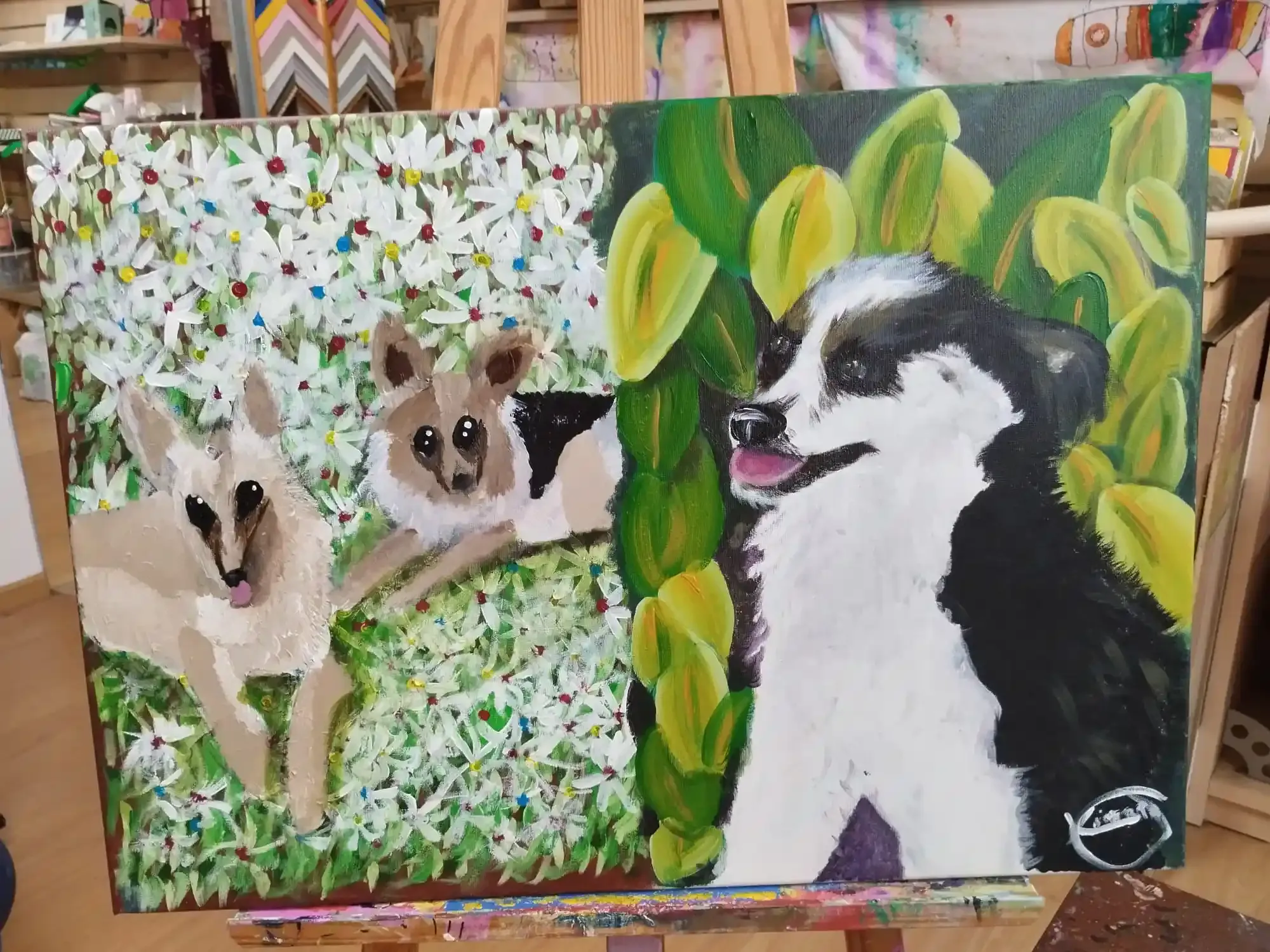 Lienzo pintado que representa a dos perros y un gato en un jardín frondoso; un perro blanco y negro aparece en primer plano.