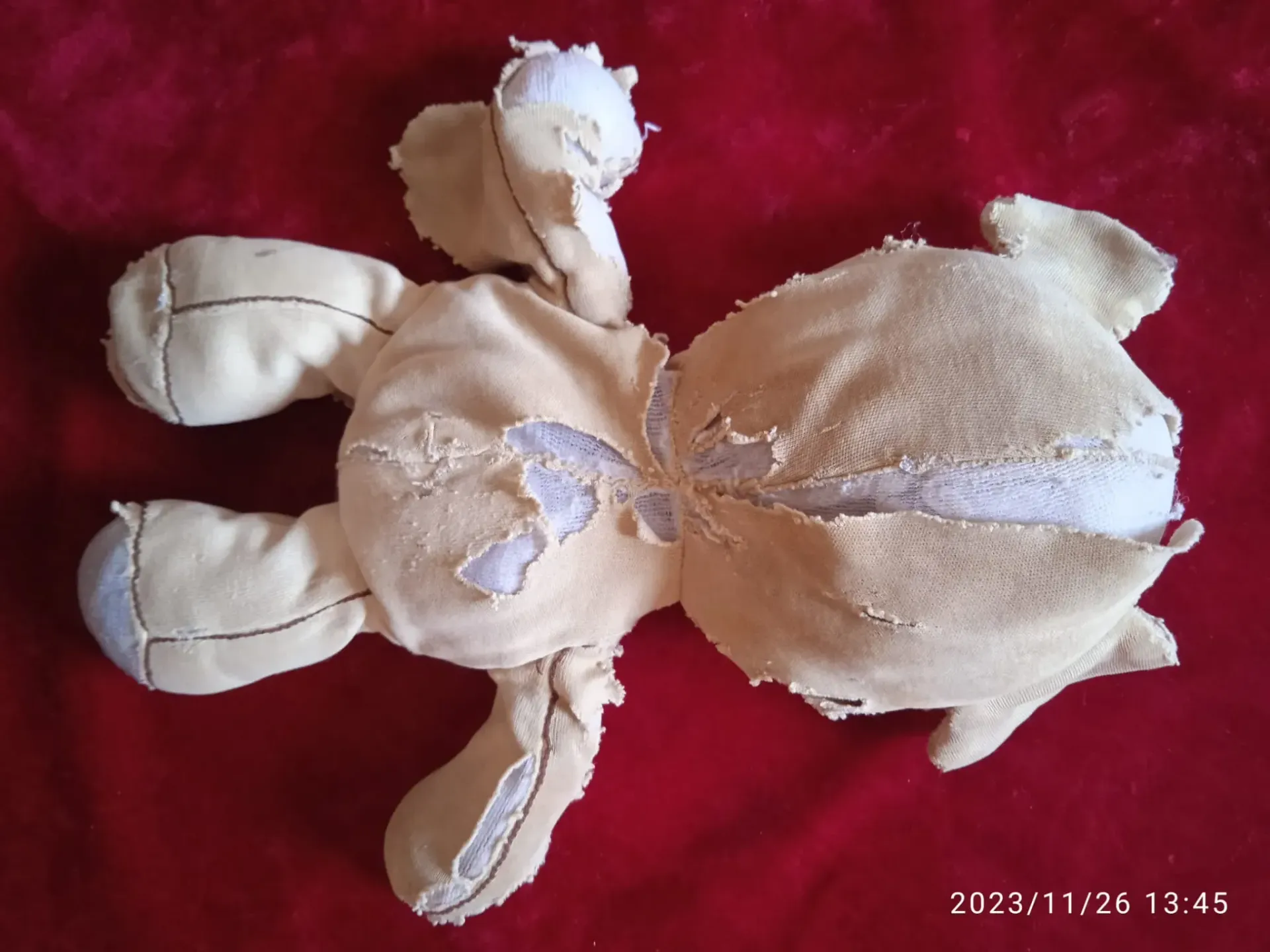 Oso de peluche beige desgastado tumbado sobre un fondo de tela roja.