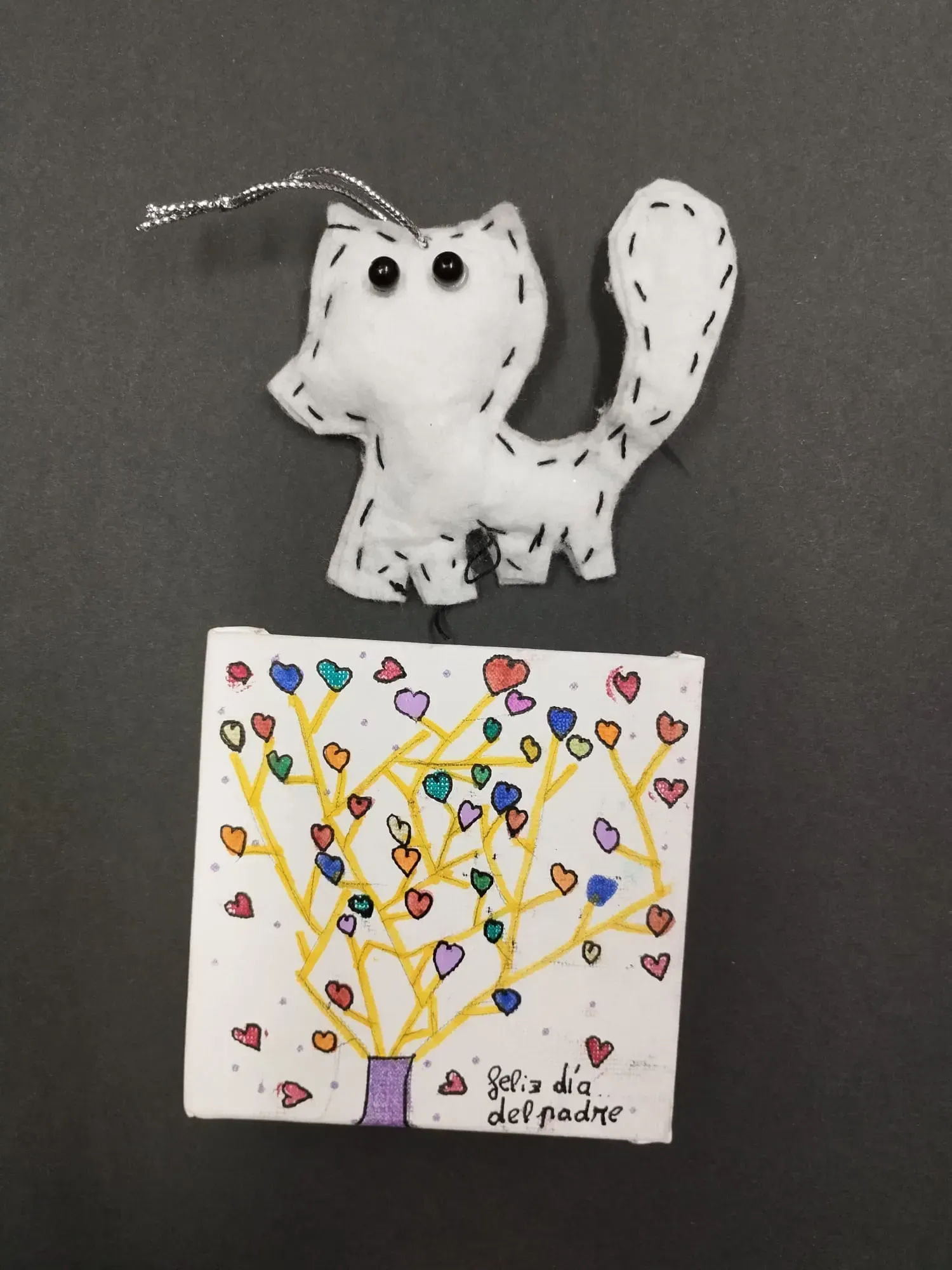 Adorno de gato blanco sobre un dibujo de un árbol cubierto de corazones de colores sobre papel.