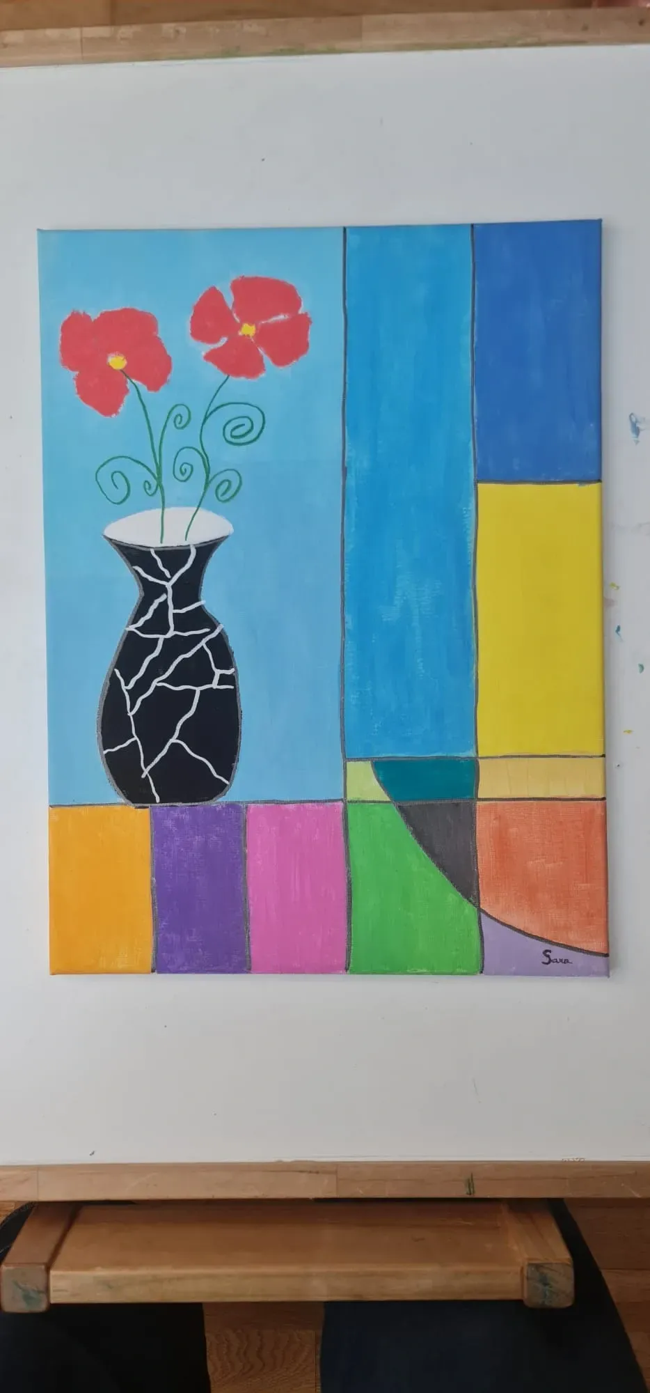 Pintura abstracta y colorida de un jarrón con flores rojas junto a bloques geométricos azules, amarillos, verdes y naranjas.