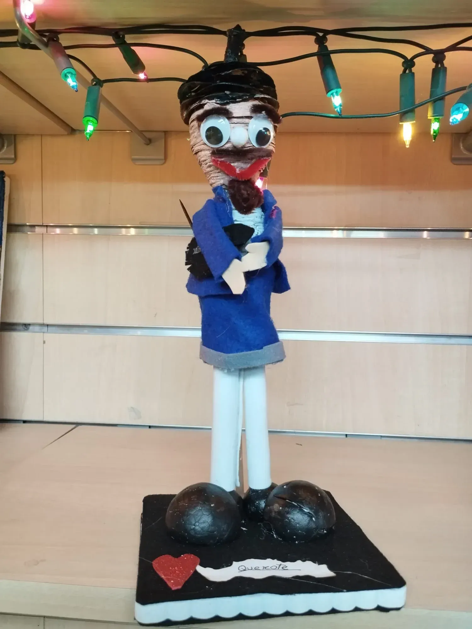 Figura de dibujos animados con chaqueta azul y sombrero negro, de pie sobre una base negra con un corazón rojo.