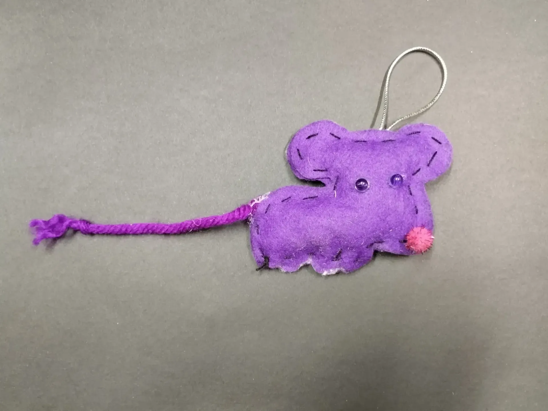 Llavero de ratón de peluche morado con argolla, sobre fondo gris.