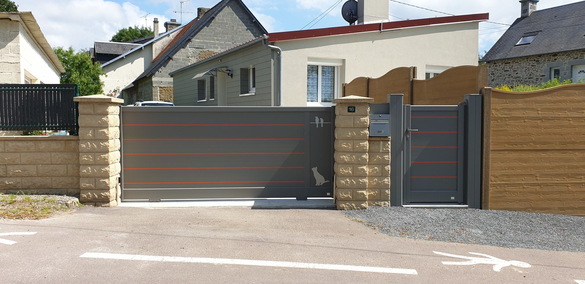 Maison résidentielle avec un grand portail gris donnant sur l’allée et une clôture en briques beiges.