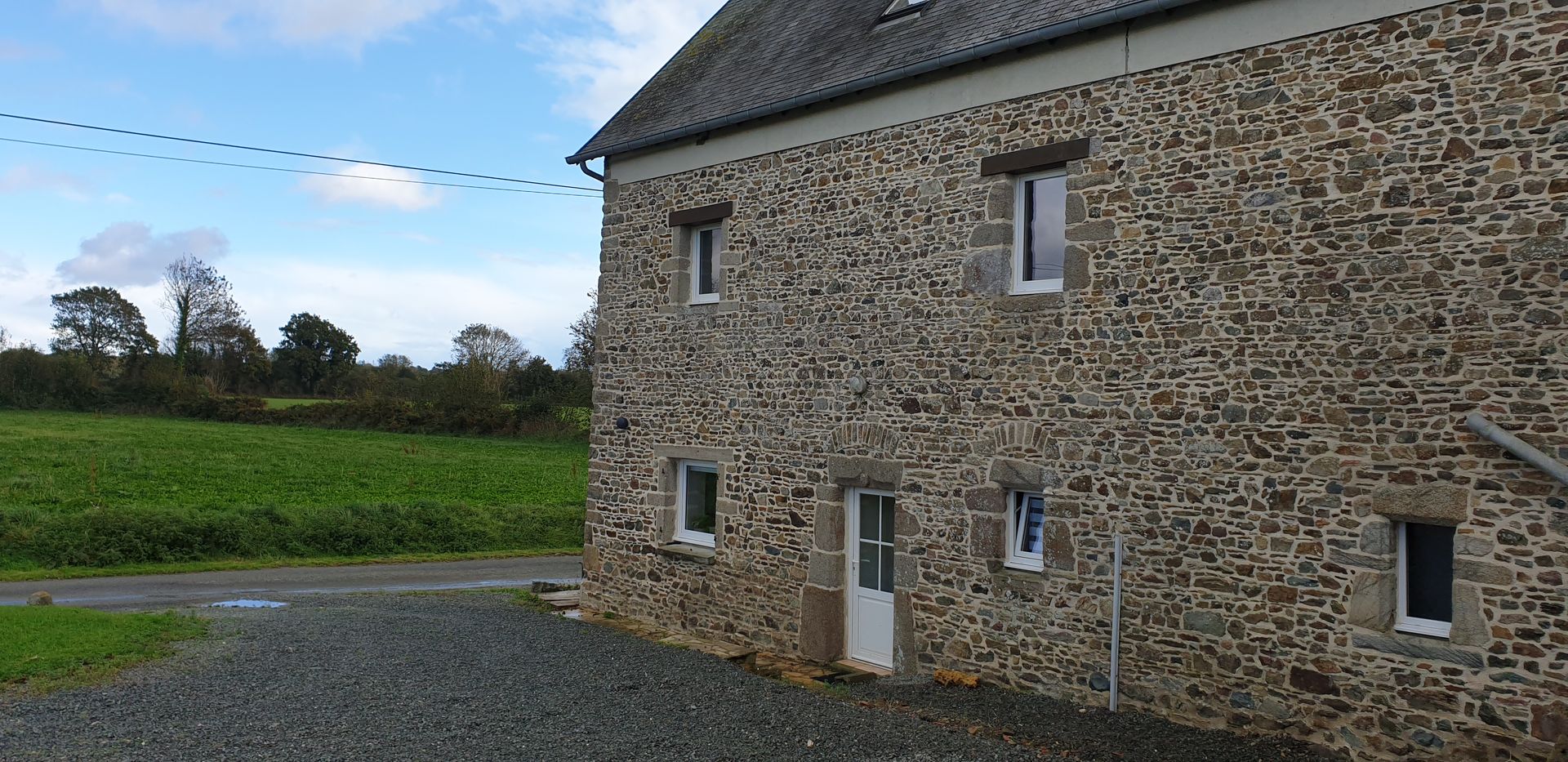 Ferme en pierre au bord d'un champ vert sous un ciel nuageux
