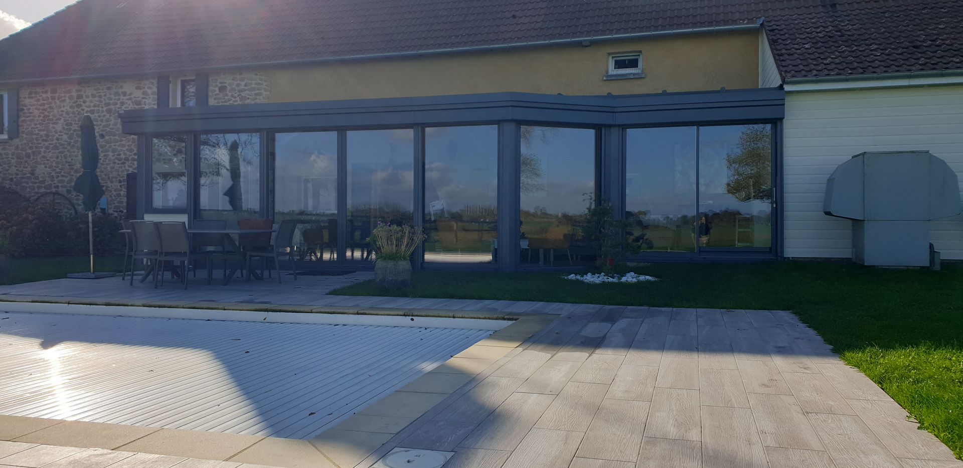 Bâtiment beige de plain-pied avec de grandes fenêtres et une terrasse devant, photographié par une journée ensoleillée.
