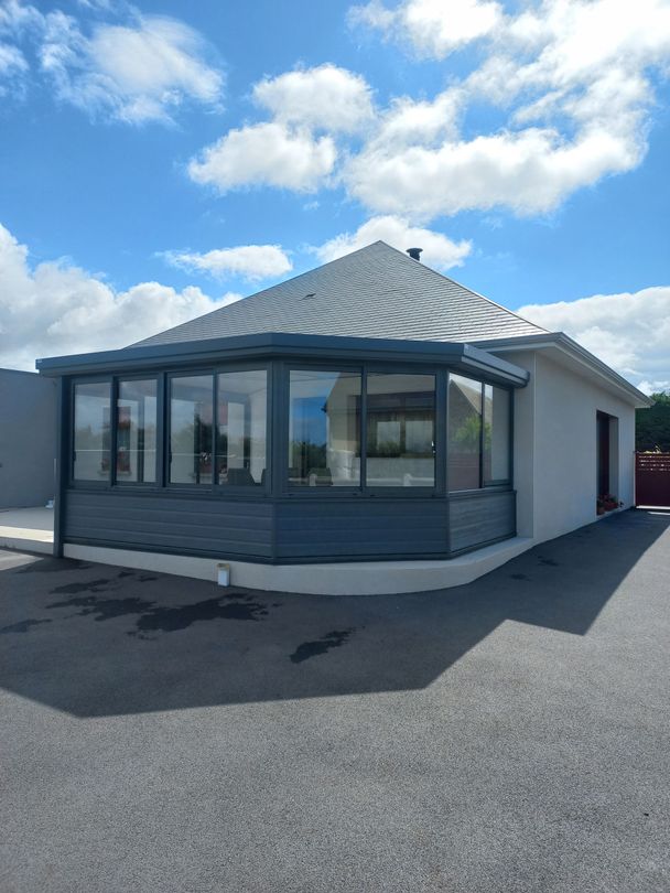 Bâtiment gris de plain-pied, avec de grandes fenêtres et un toit arrondi, sous un ciel bleu.