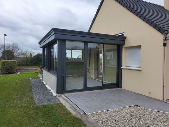 Maison blanche moderne avec un patio vitré foncé et une terrasse pavée