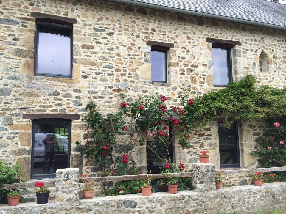 Façade en pierre d'une maison avec des roses rouges, des vignes vertes et des plantes en pot le long du rebord de la fenêtre