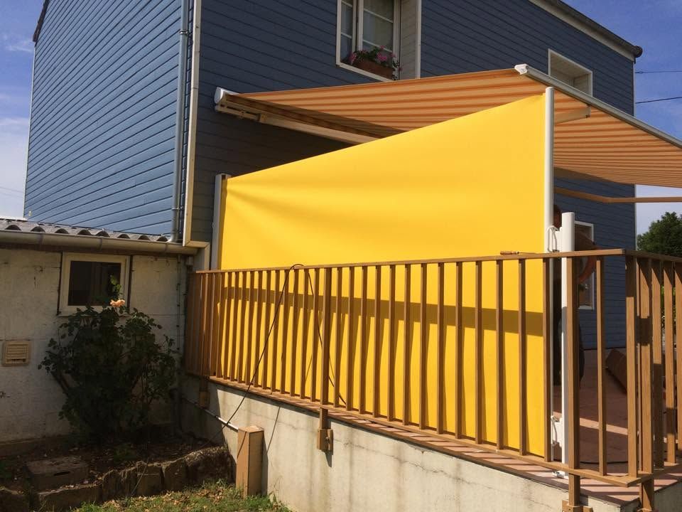 Auvent jaune de terrasse à côté d'une maison avec une clôture en bois et un bardage bleu.