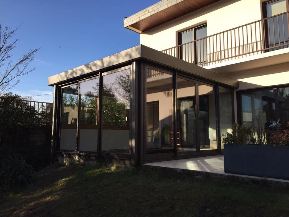 Patio d'une maison moderne avec murs de verre, balcon et jardin ensoleillé au crépuscule