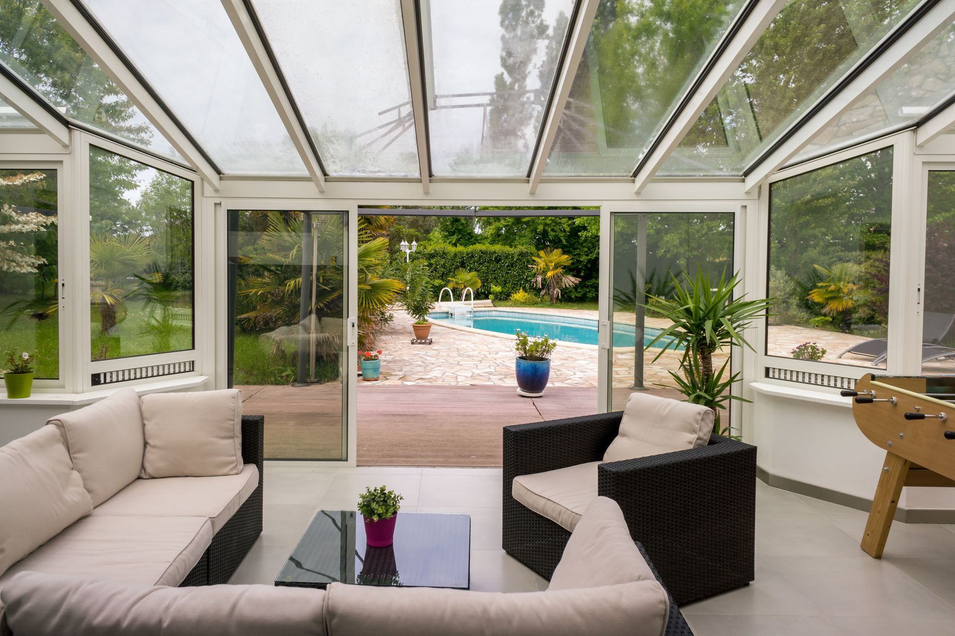 Véranda lumineuse avec canapés beiges donnant sur un jardin et une piscine