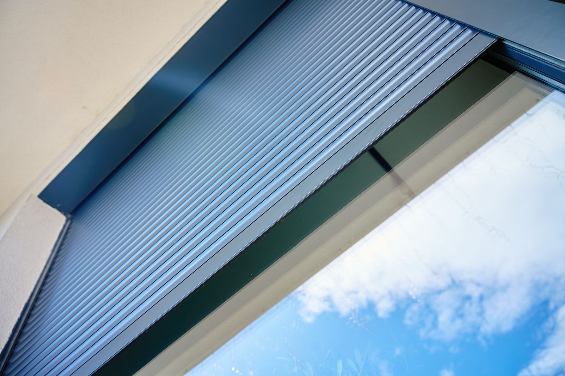 Store bleu partiellement baissé sur une fenêtre donnant sur le ciel.
