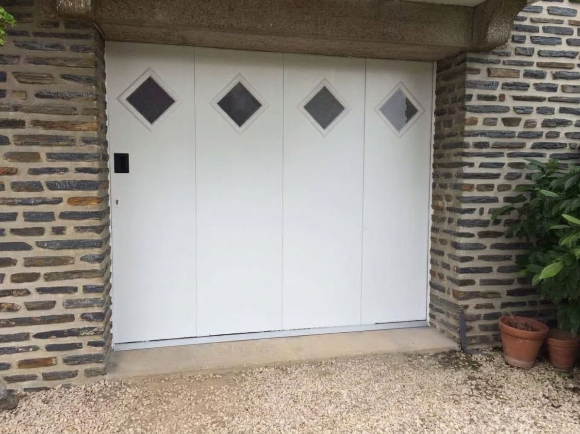 Portes de garage blanches encastrées dans un mur de briques, avec fenêtres en losange.