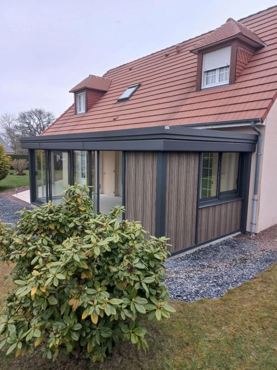 Maison moderne avec un toit en tuiles rouges, un bardage en bois et de grandes fenêtres, au bord d’une allée en gravier