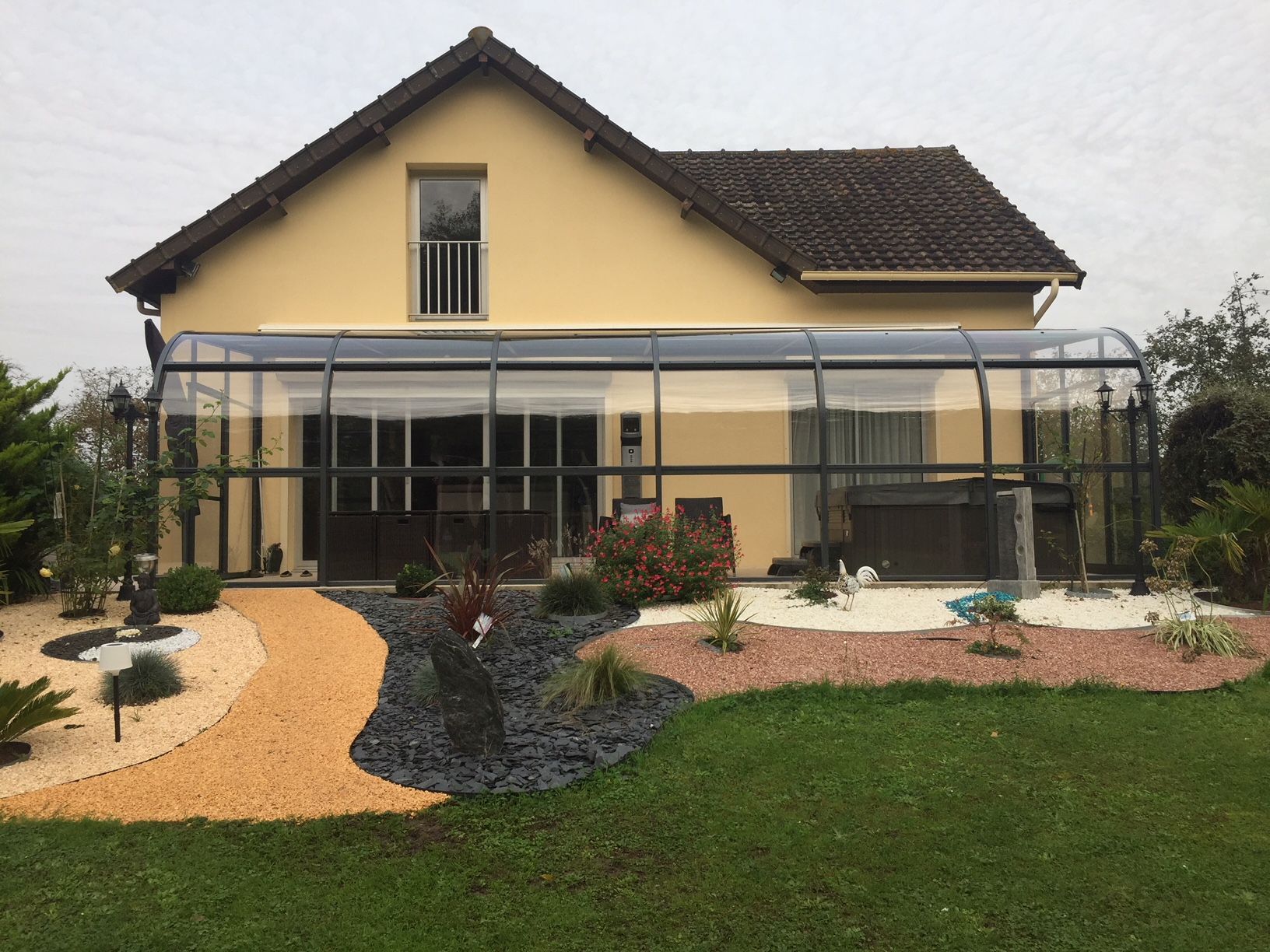 Maison beige à deux étages avec patio couvert, cour avant paysagée et chemin de gravier incurvé