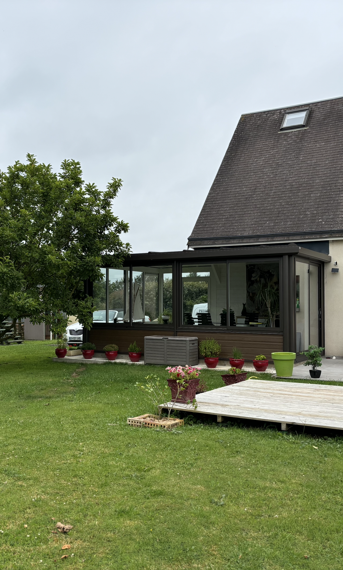 Maison moderne avec un toit sombre, une véranda vitrée et une pelouse verte au premier plan.