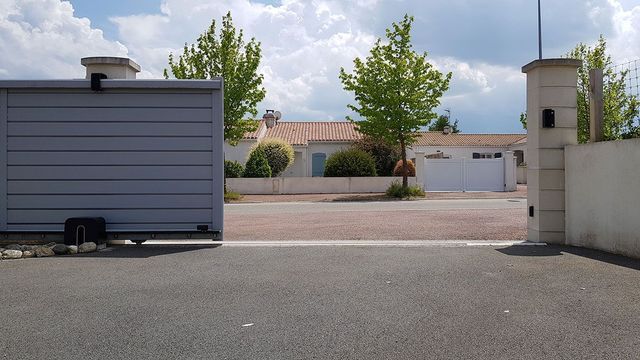 Parking vide à côté d'un bâtiment gris et d'un mur blanc sous un ciel partiellement nuageux