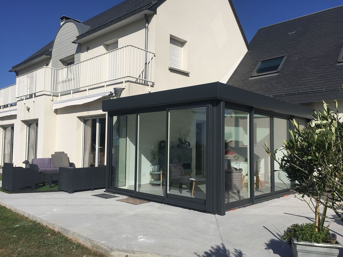 Maison blanche moderne avec un patio vitré foncé et une terrasse pavée