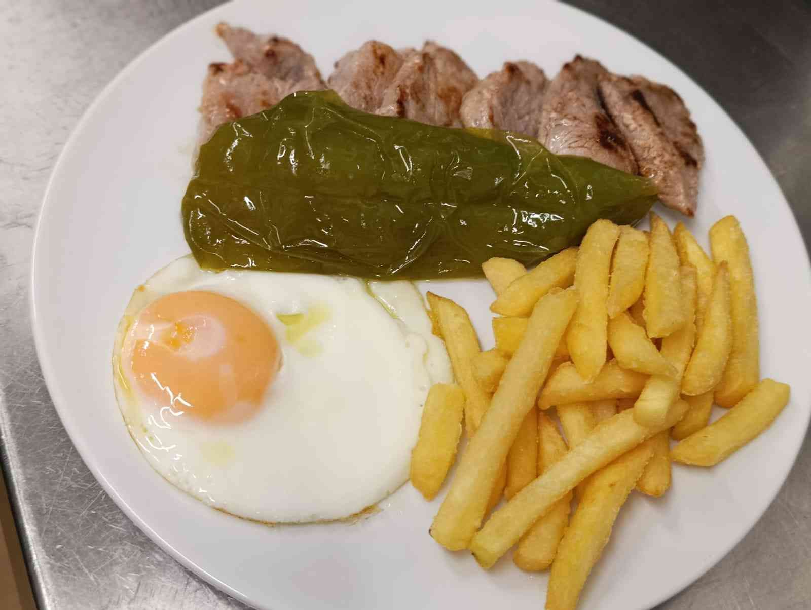 Plato con cerdo a la parrilla, un pimiento verde, un huevo frito y patatas fritas.