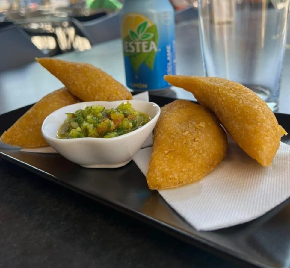 Pan tostado cubierto con rodajas de tomate y aguacate, sobre un plato con condimentos.