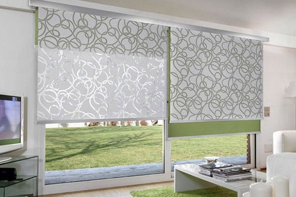 Persianas de doble capa, de tela estampada verde y blanca, delante de una puerta de cristal con vistas al césped.