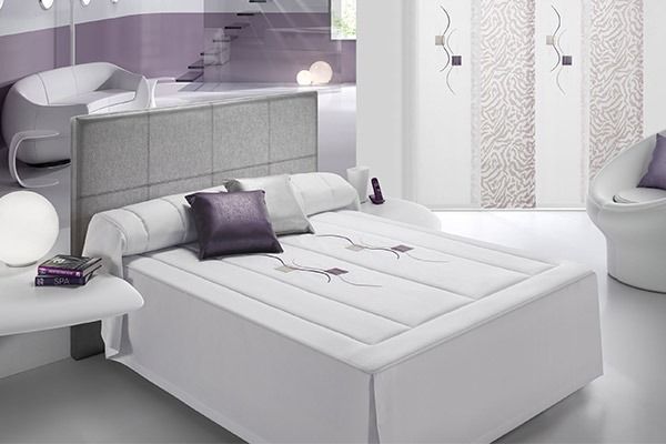 Dormitorio moderno en color blanco con detalles en lavanda y cabecero tapizado.
