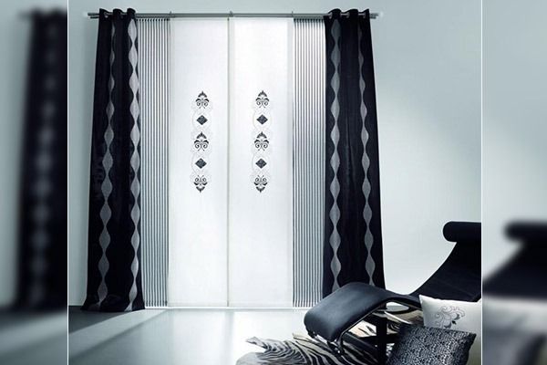 Cortinas blancas y negras en una ventana. Un diván está delante de la ventana.