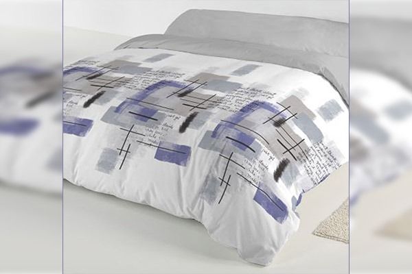 Edredón blanco con estampado geométrico azul, gris y negro, con la parte superior gris, sobre una cama.