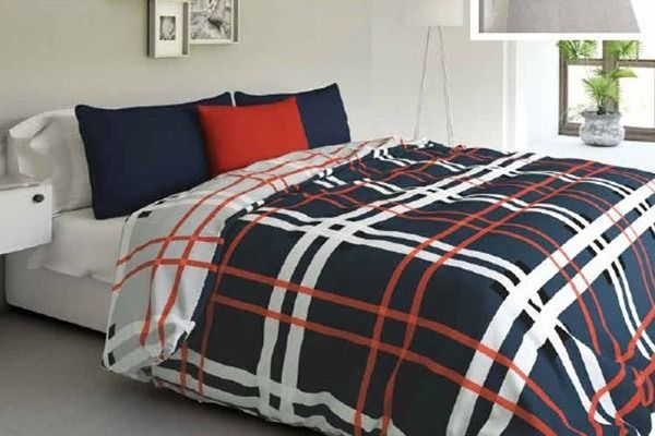 Cama con edredón a cuadros azul marino, blanco y rojo, almohadas y ropa de cama blanca.