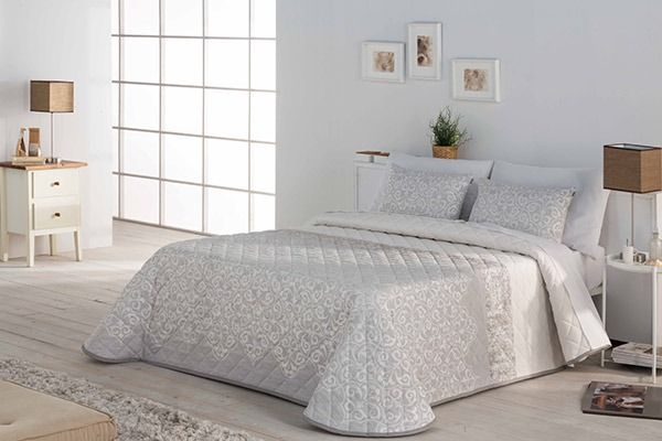 Dormitorio con ropa de cama y muebles blancos y de colores claros. Iluminado por el sol a través de una gran ventana.