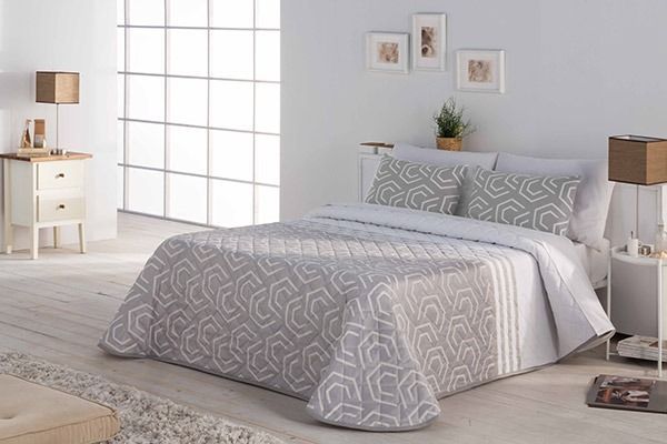 Dormitorio con colcha gris y blanca, dos almohadas a juego, mesitas de noche, lámparas y obras de arte.