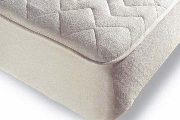 Primer plano de un protector de colchón acolchado blanco sobre una cama con una falda de cama a juego.