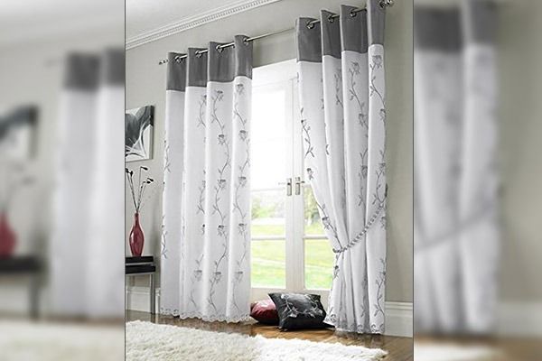 Cortinas blancas traslúcidas con ribete gris y bordado floral, que enmarcan una ventana.