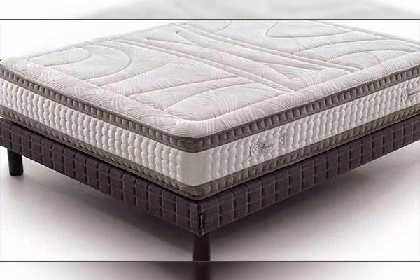 Colchón sobre una base oscura con estampado cuadrado. El colchón es blanco con borde y costuras grises.