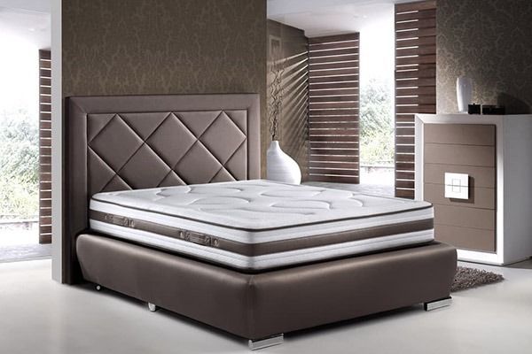 Cama tapizada en marrón con cabecero estampado de rombos, colchón blanco y mesita de noche a juego.