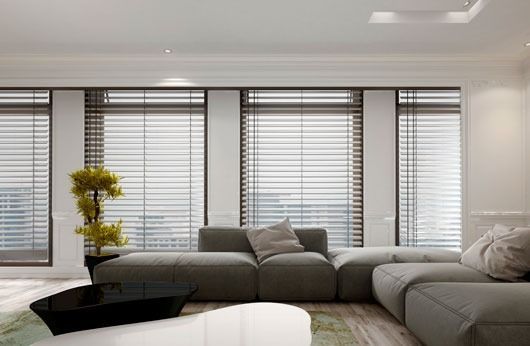 Sala de estar con sofá seccional gris, grandes ventanas con persianas y una mesa de centro negra.