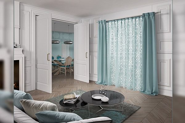 Cortinas color verde azulado en una sala de estar con una mesa de centro redonda y puertas abiertas que dan a un comedor.