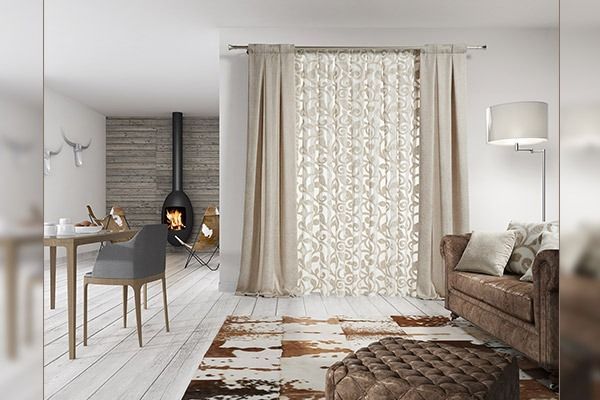 Acogedor salón con cortinas beige, sofá de cuero marrón y alfombra estampada. Se ven la chimenea y la mesa de comedor.