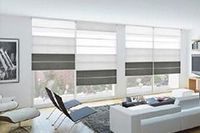 Salón con estores romanos blancos y grises en grandes ventanales, mobiliario moderno.