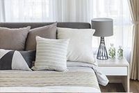 Cama con almohadas, una lámpara y una mesita de noche delante de una cortina transparente.