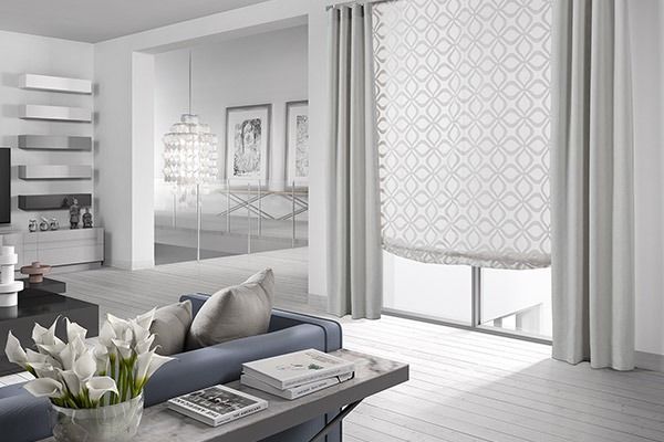 Salón moderno con sofá azul, cortinas gris claro, persiana estampada y paredes blancas.